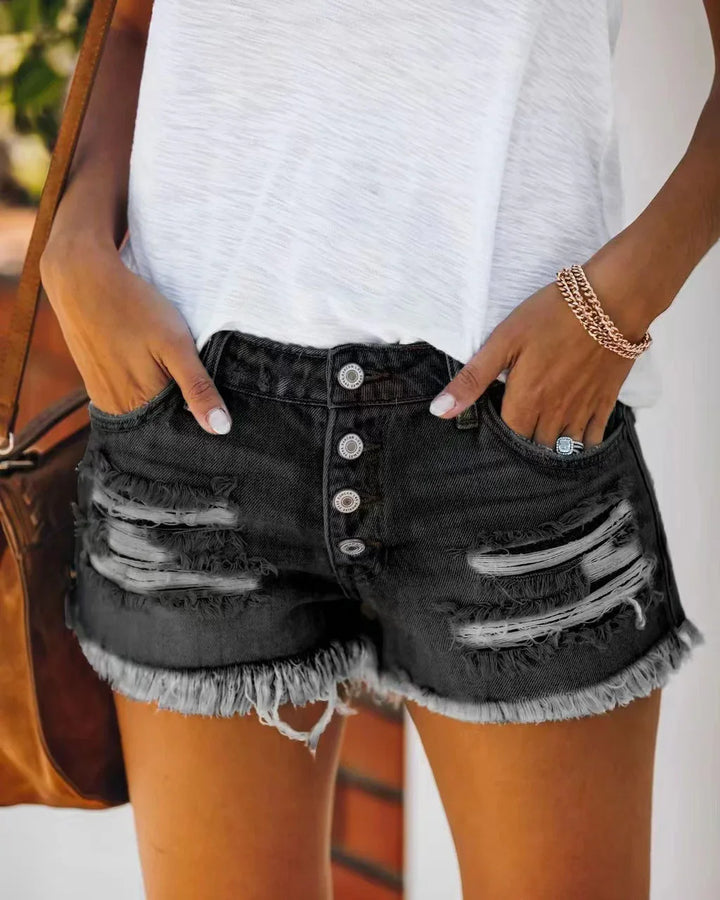 Woman wearing distressed black denim shorts with button fly and white top, casual summer outfit