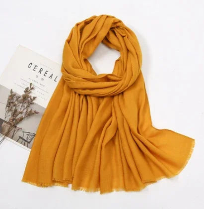 Mustard yellow soft scarf displayed with a magazine and dried flowers on a white background