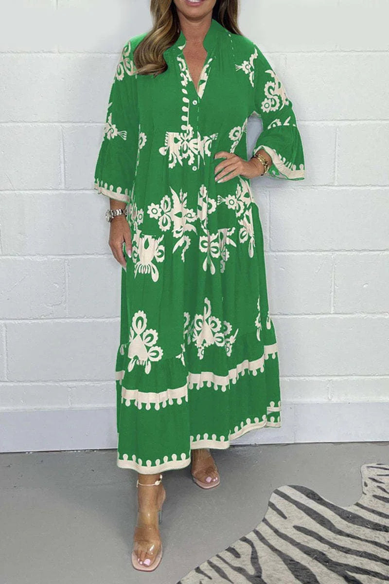 Woman wearing green maxi dress with white floral patterns and bell sleeves standing against white brick wall