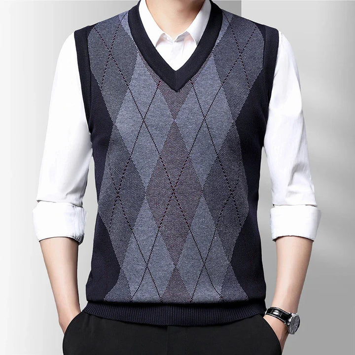 Man wearing navy blue and gray argyle V-neck sweater vest over white shirt with sleeves rolled up