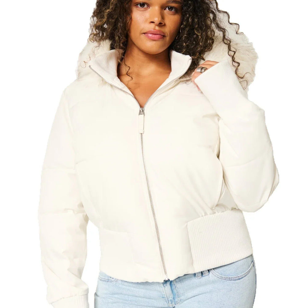 Woman wearing white puffer jacket with fur-trimmed hood and ribbed cuff, paired with light blue jeans