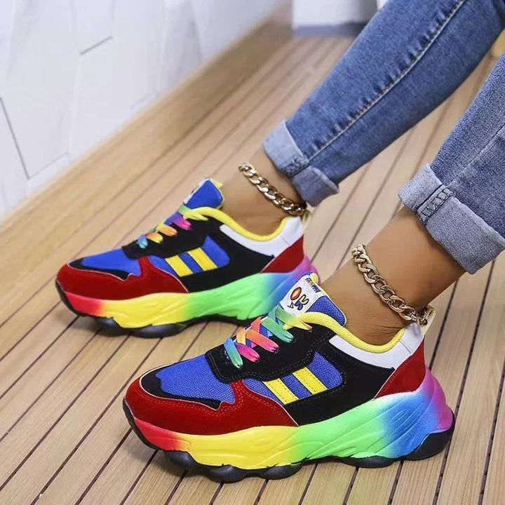 Colorful women's sneakers with rainbow soles, blue and red uppers, yellow stripes, paired with rolled jeans and gold anklets