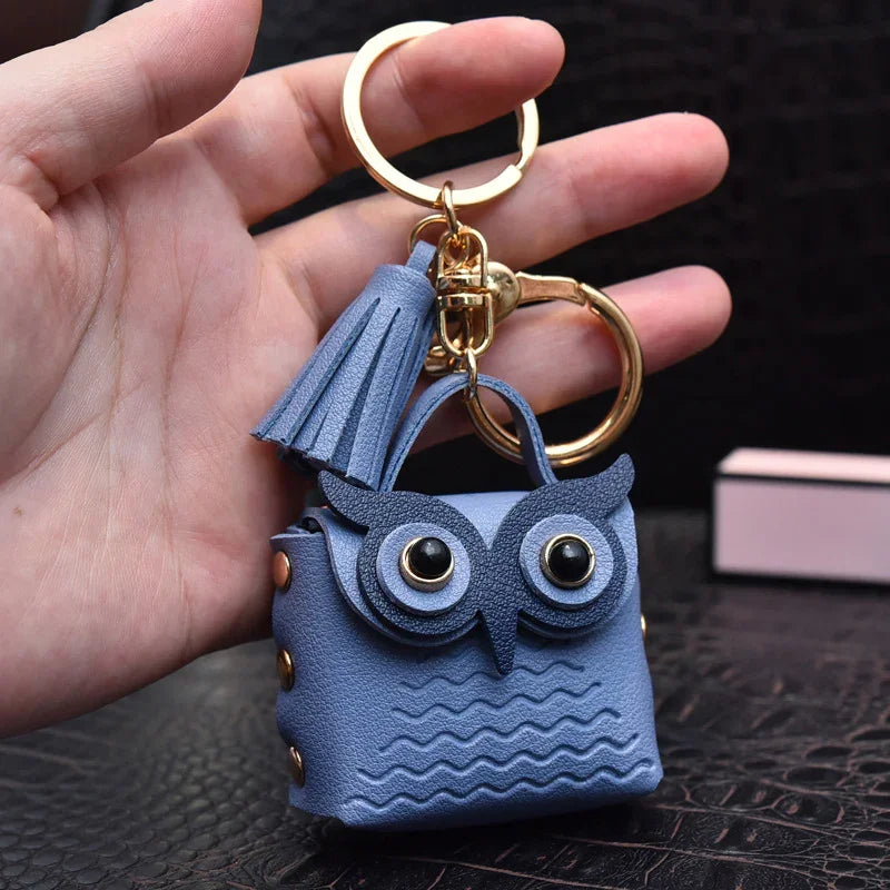 Blue owl-shaped leather keychain with tassel held in hand against black background