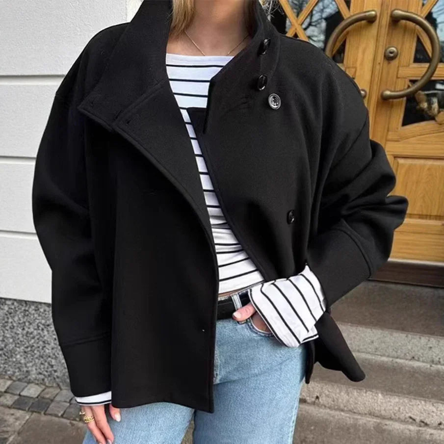 Woman wearing black buttoned coat over striped long sleeve top with blue jeans near wooden door
