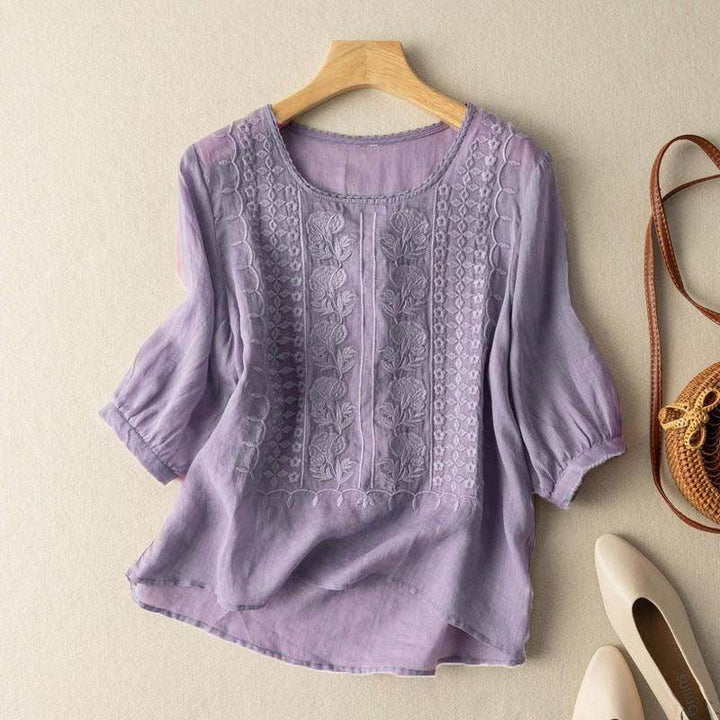 Light purple linen blouse with floral embroidery on front, half sleeves, displayed on wooden hanger