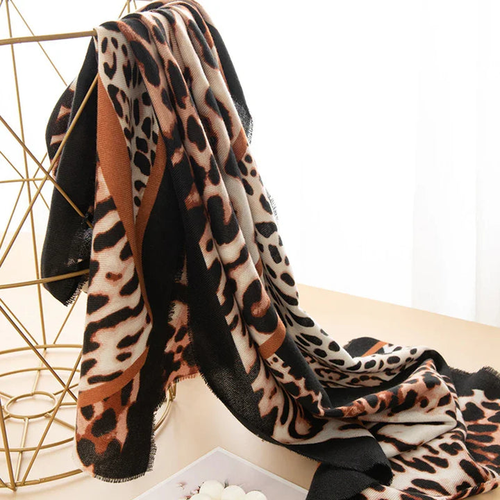 Leopard print scarf draped on gold geometric metal stand on beige surface with soft natural light
