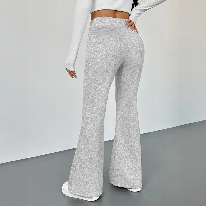 Woman wearing light grey wide-leg lounge pants and white cropped top against plain backdrop