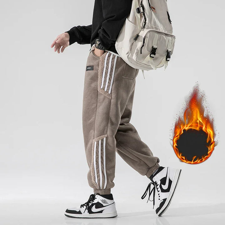 Person wearing beige fleece jogger pants with white stripes, black sweatshirt, white backpack, and black white sneakers