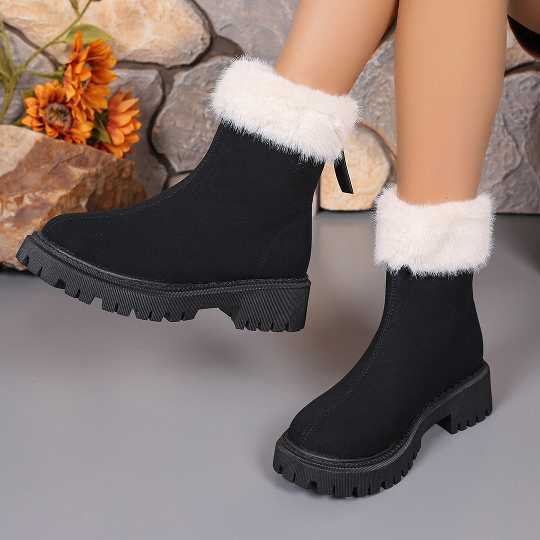 Black winter boots with thick soles and white faux fur cuffs on gray floor with stone and orange flowers background