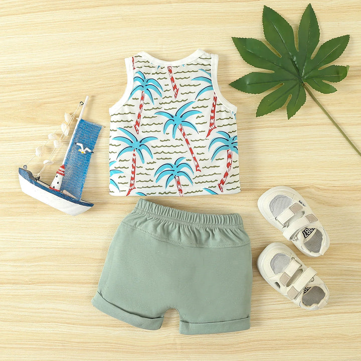 Toddler summer outfit with palm tree tank top, green shorts, white sandals, toy sailboat, and large green leaf