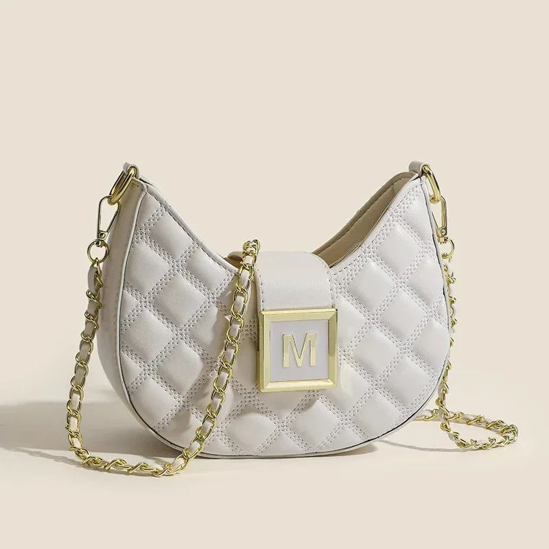 White quilted leather handbag with gold chain strap and gold M logo clasp on beige background