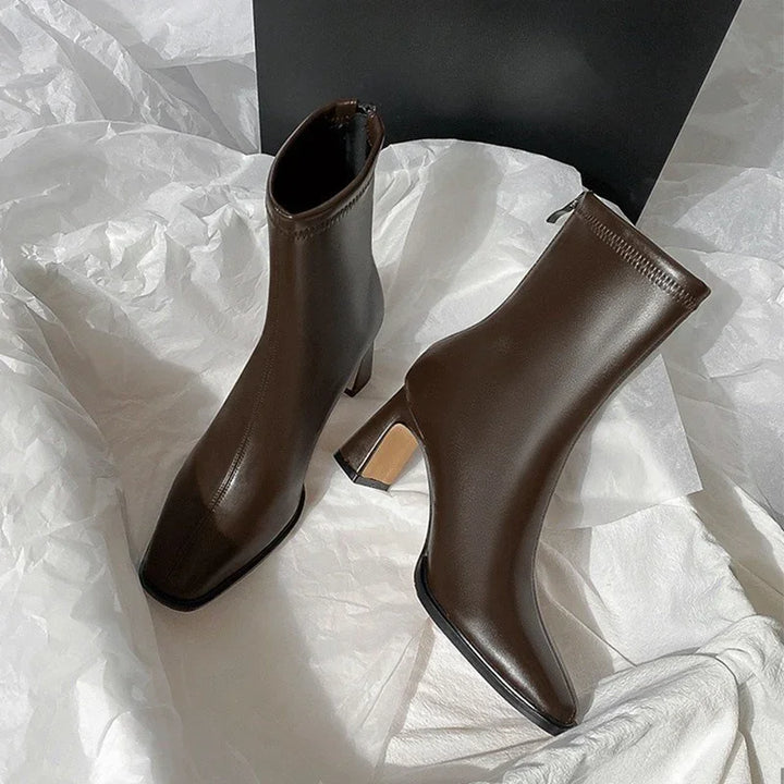 Pair of sleek dark brown leather ankle boots with block heels on white fabric