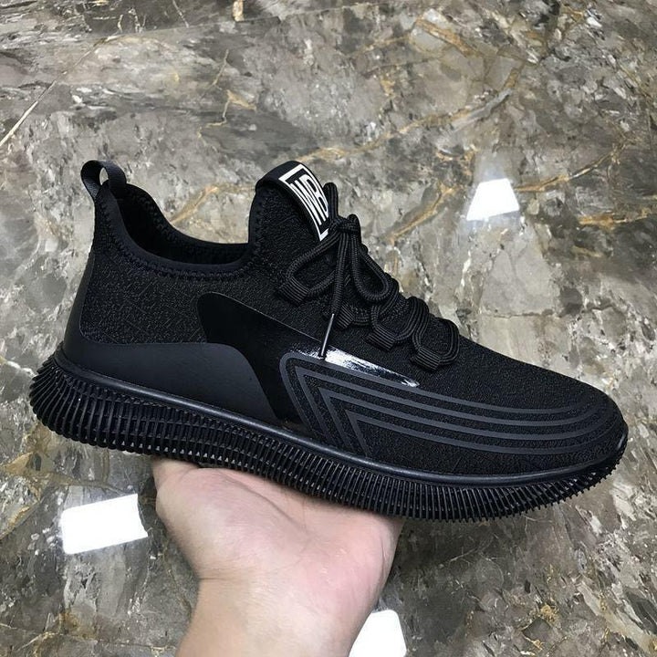 Hand holding black athletic sneaker with textured sole and geometric stripe design on marble floor