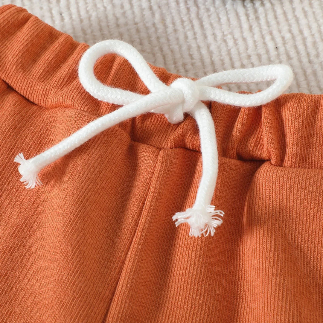 Close-up of burnt orange cotton pants with white drawstring bow on ribbed texture fabric