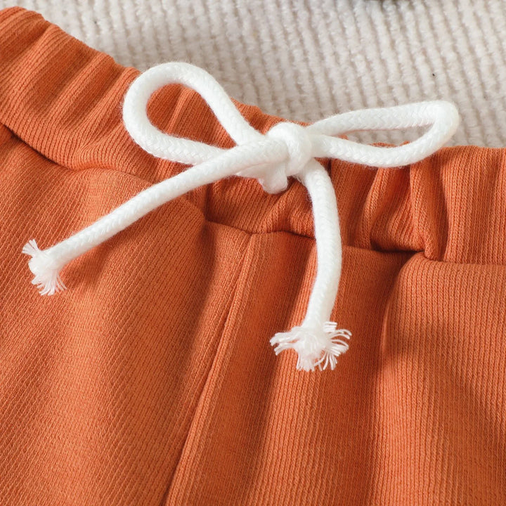 Close-up of burnt orange cotton pants with white drawstring bow on ribbed texture fabric