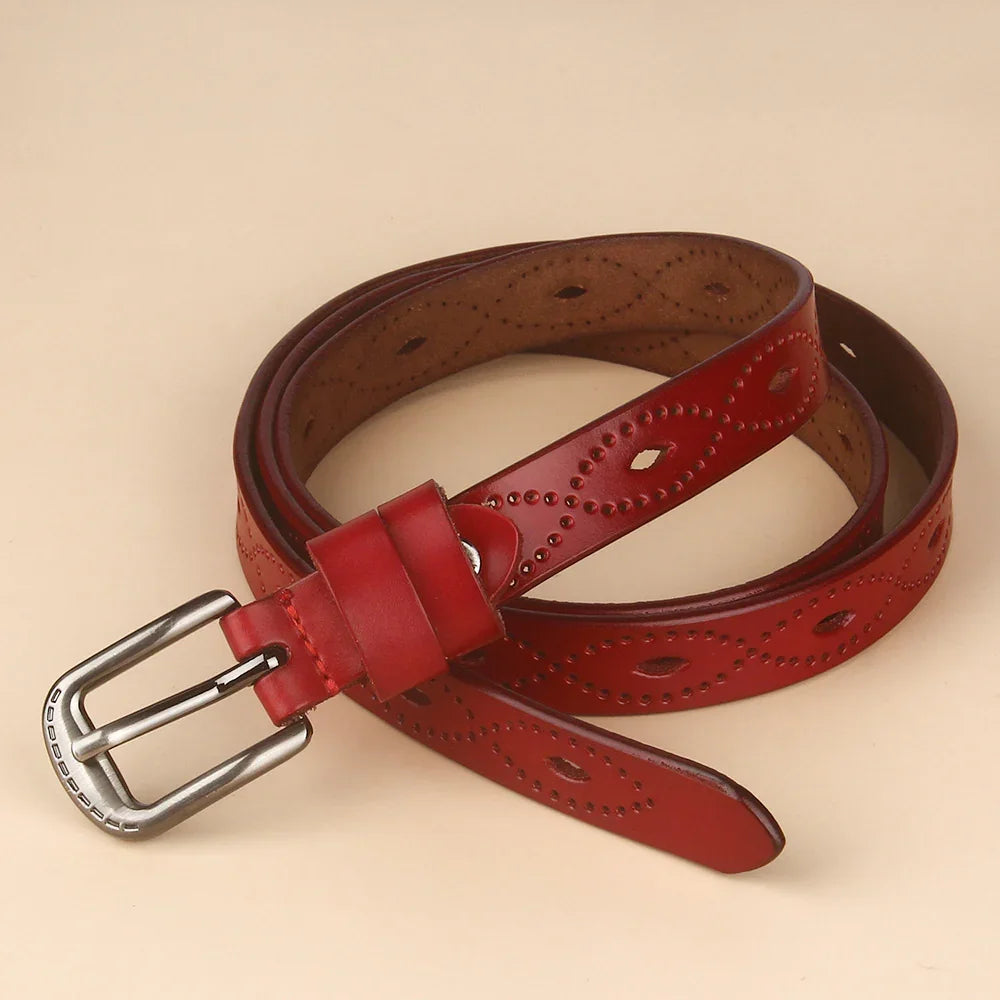 Red leather belt with decorative perforations and metal buckle on beige background