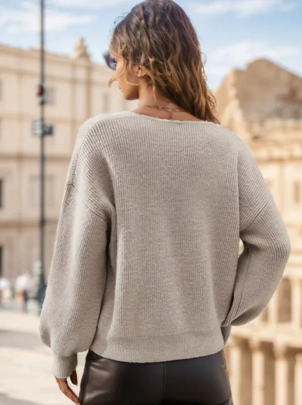 Woman wearing beige knit sweater and black leather pants standing outdoors with blurred historic buildings in background