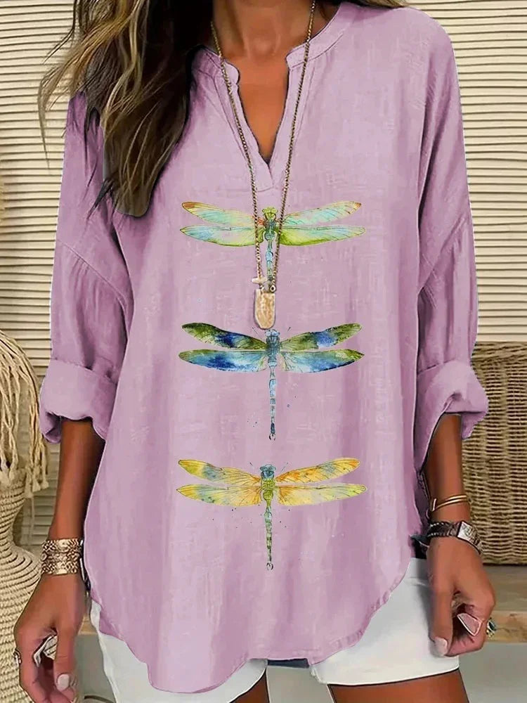 Woman wearing lavender blouse with colorful dragonfly prints and rolled sleeves, accessorized with layered necklaces and bracelets
