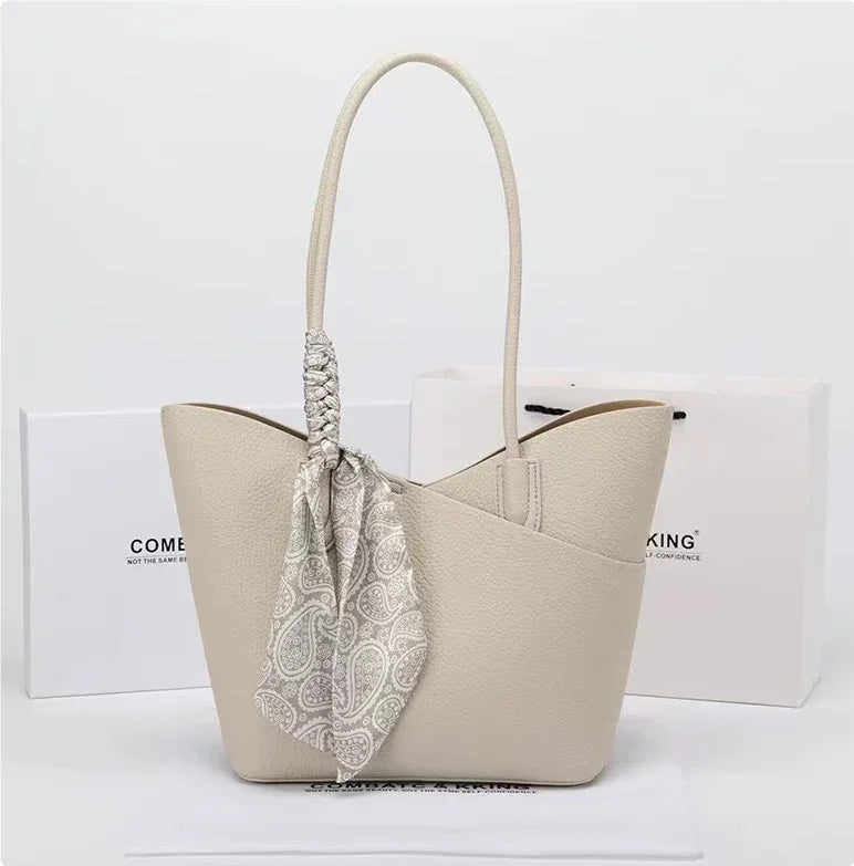 Beige textured leather handbag with paisley scarf detail and long handles on white background