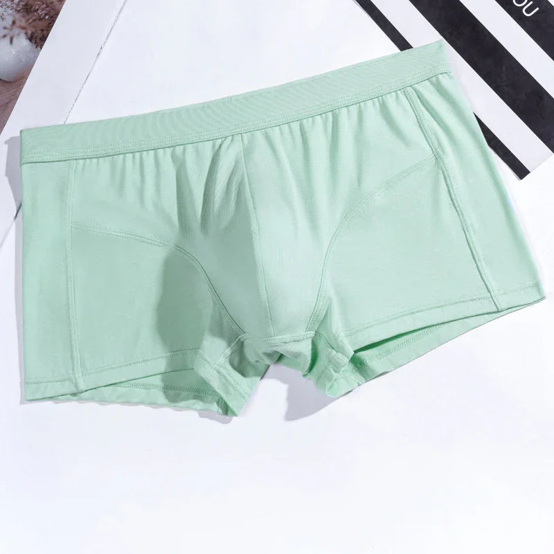 Light green men's boxer briefs on a white surface with black and white paper corner