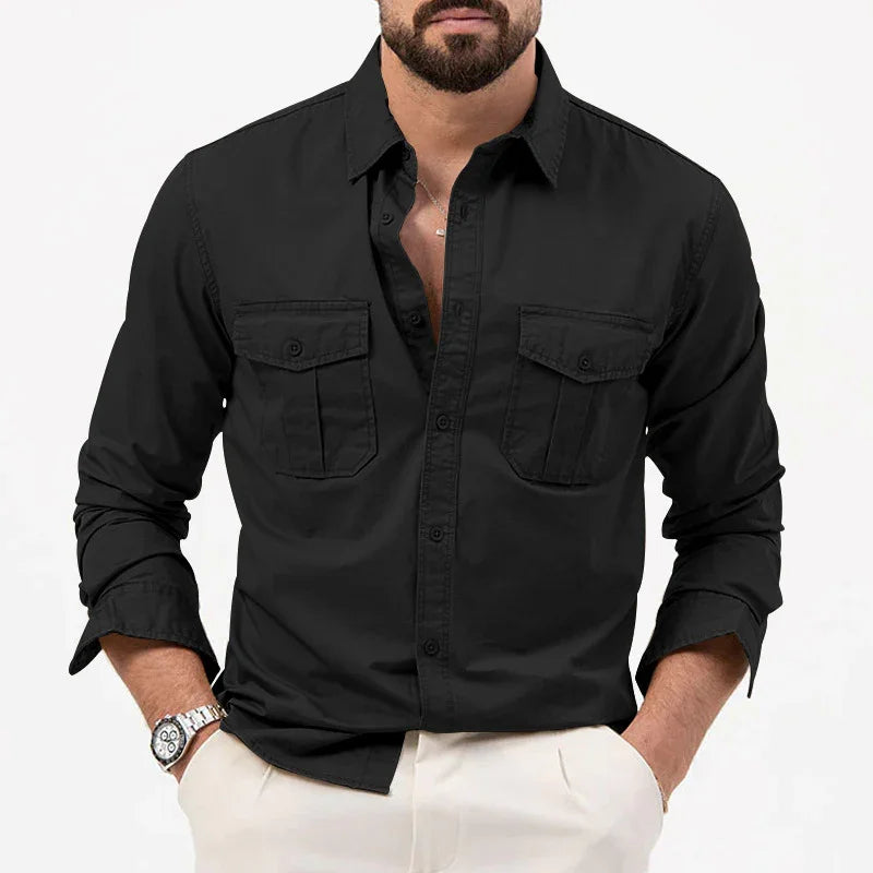 Man wearing black button-up shirt with two chest pockets and white pants, accessorized with watch and necklace
