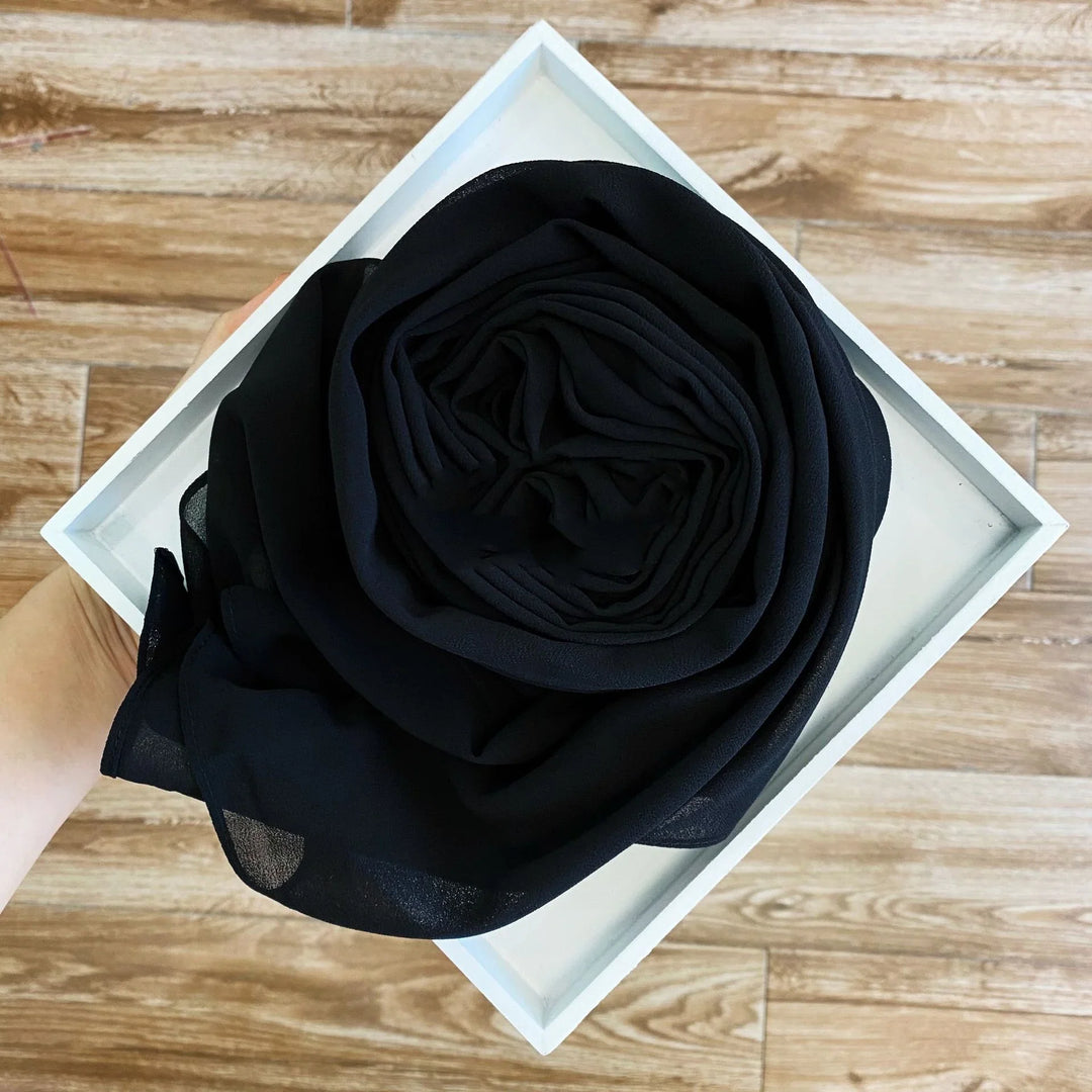 Hand holding white box with neatly folded black chiffon fabric on wooden floor