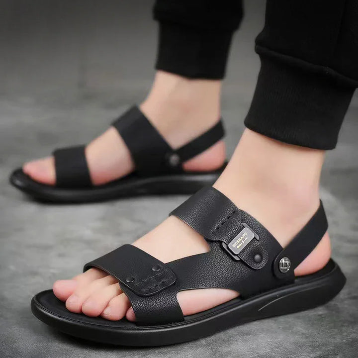 close-up of black leather men's sandals with wide straps and metal buckle on gray floor