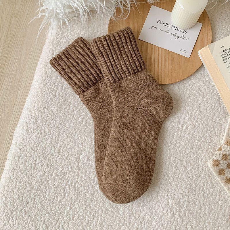 Pair of cozy brown wool socks with ribbed cuffs on a textured white blanket, next to a candle and book