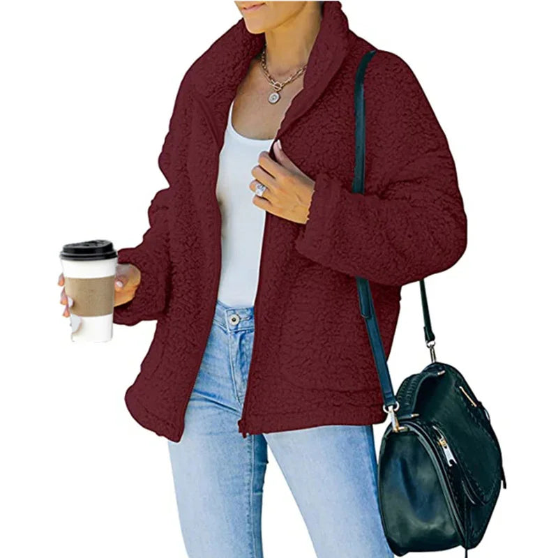 Woman wearing a cozy maroon sherpa jacket, white tank top, light blue jeans, holding coffee cup, black shoulder bag