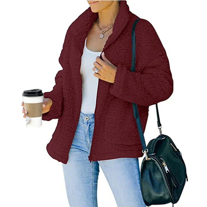 Woman wearing a cozy maroon sherpa jacket, white tank top, light blue jeans, holding coffee cup, black shoulder bag