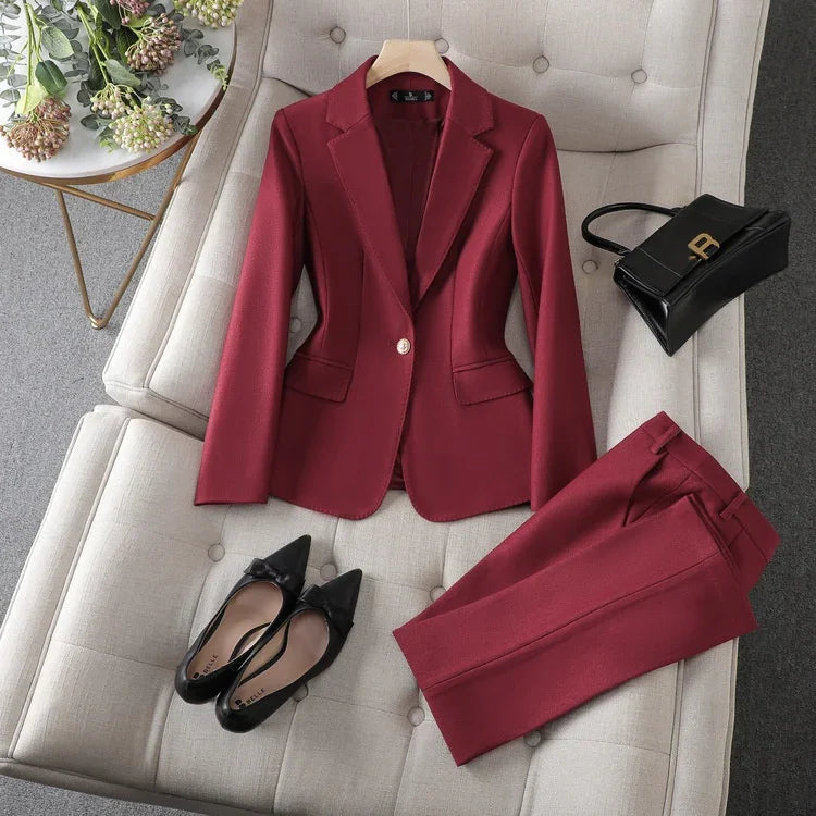Red women's tailored blazer and matching pants on beige tufted sofa with black pointed flats and black handbag