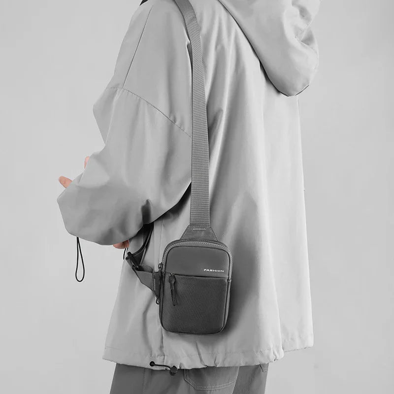 Person wearing gray jacket carrying small black crossbody bag with adjustable strap