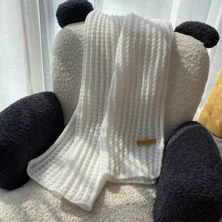 White handmade knit blanket draped over black and white teddy bear armchair near sheer curtains