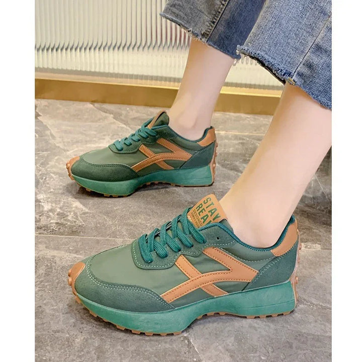 Green and brown casual sneakers with thick sole worn with cropped blue jeans on gray tile floor