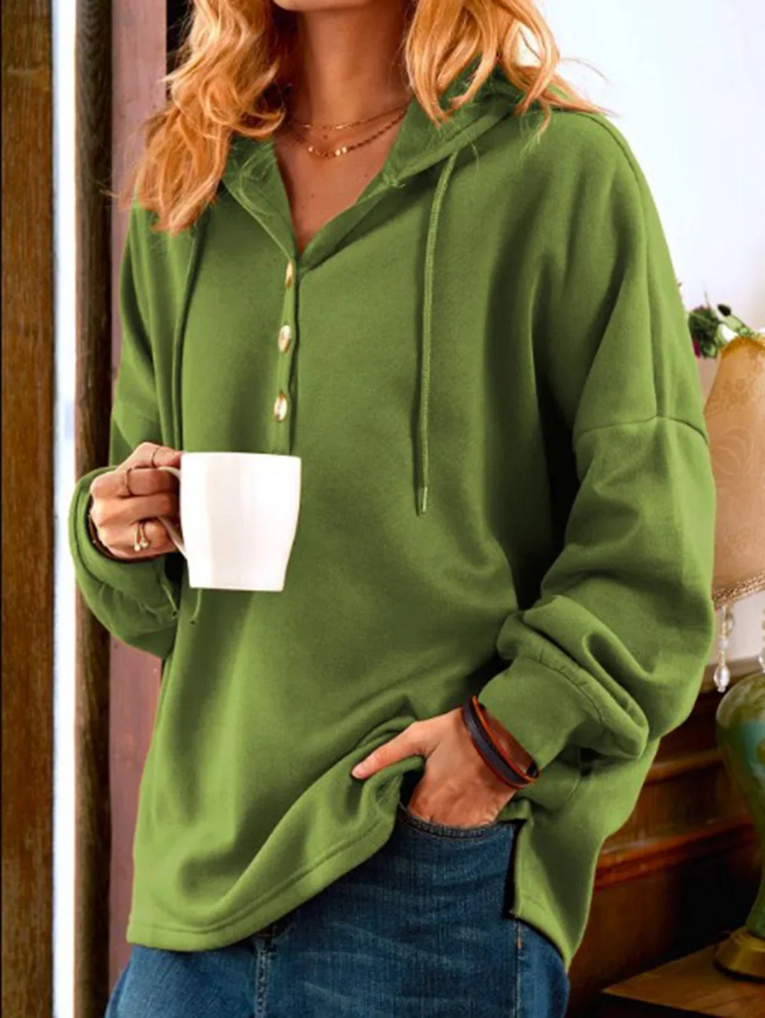 Woman in green hooded pullover with buttons holding white mug, casual cozy indoor outfit