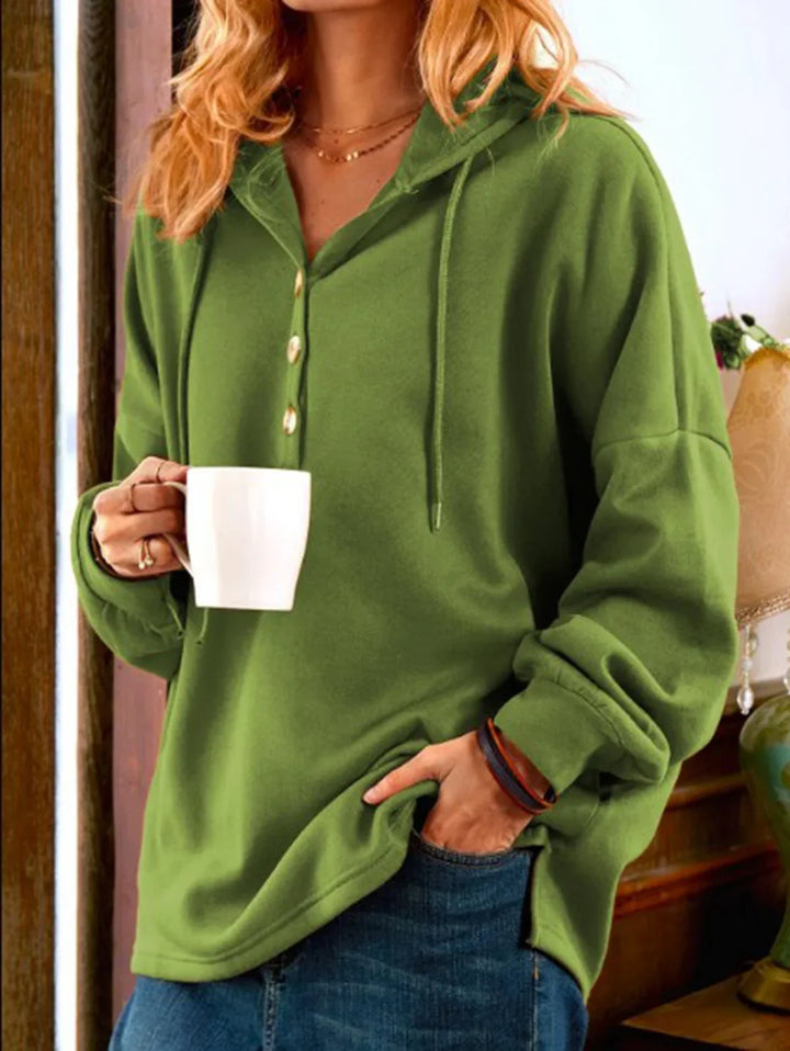 Woman in green hooded pullover with buttons holding white mug, casual cozy indoor outfit