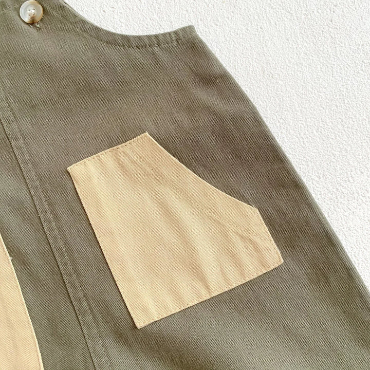 Close-up of olive green garment with beige angled pocket and cream button on textured white background