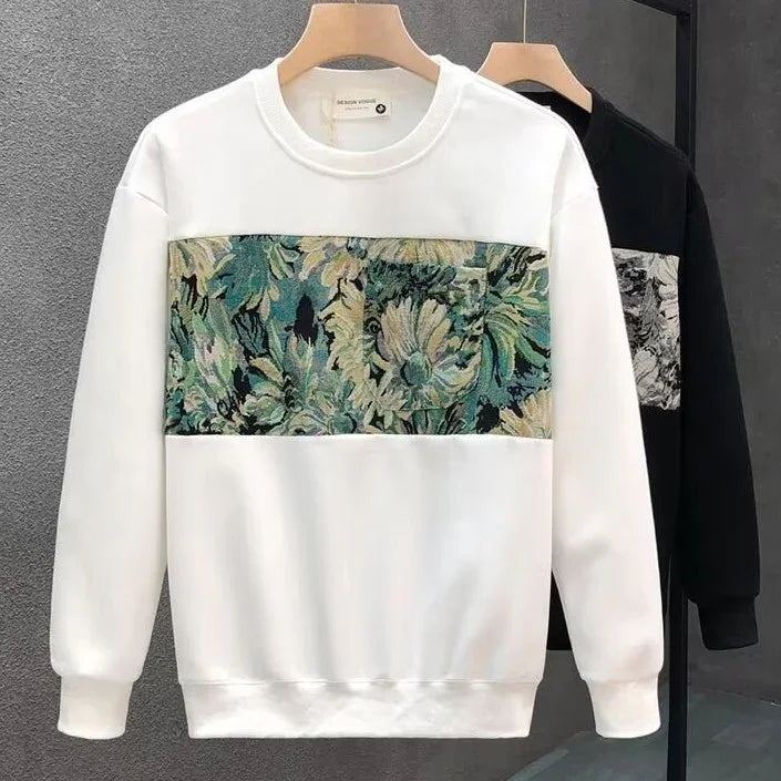 White sweatshirt with green and beige floral tapestry pattern on chest and pocket, hanging on wooden hanger