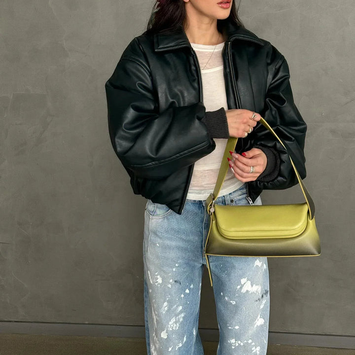 Woman wearing a black puffer jacket and distressed jeans holding a stylish olive green shoulder bag