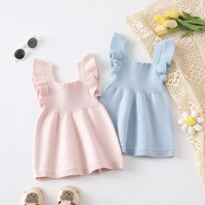 Two knitted baby dresses in pastel pink and blue with ruffled sleeves on white background