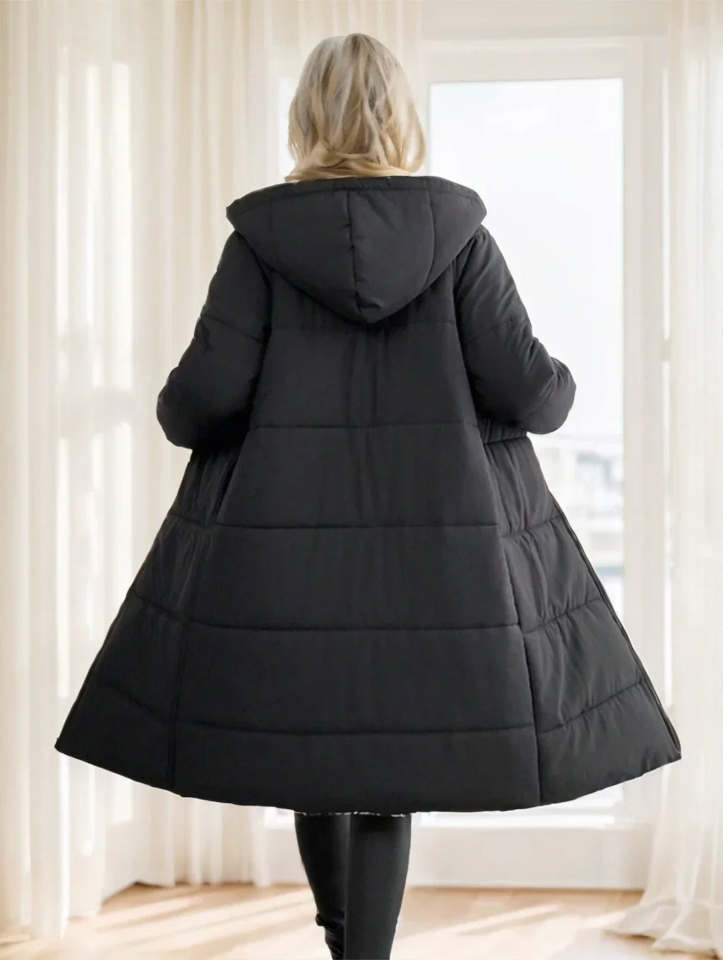 Back view of woman wearing long black puffer coat with hood standing indoors
