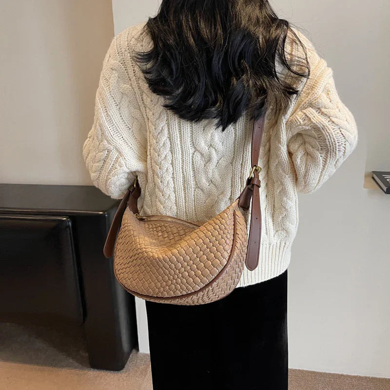 Woman wearing cream cable knit sweater with woven tan leather shoulder bag indoors