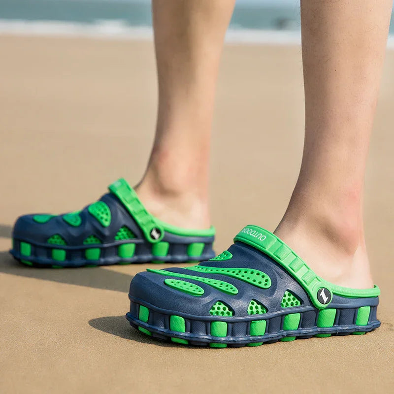 Person wearing navy blue and green outdoor slip-on clogs standing on sandy beach
