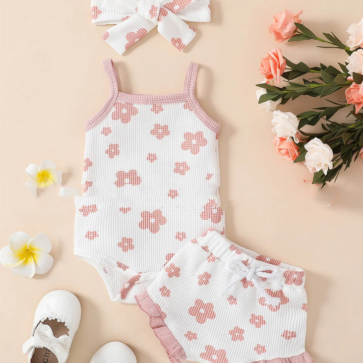 White and pink floral baby romper with matching shorts and headband on beige background