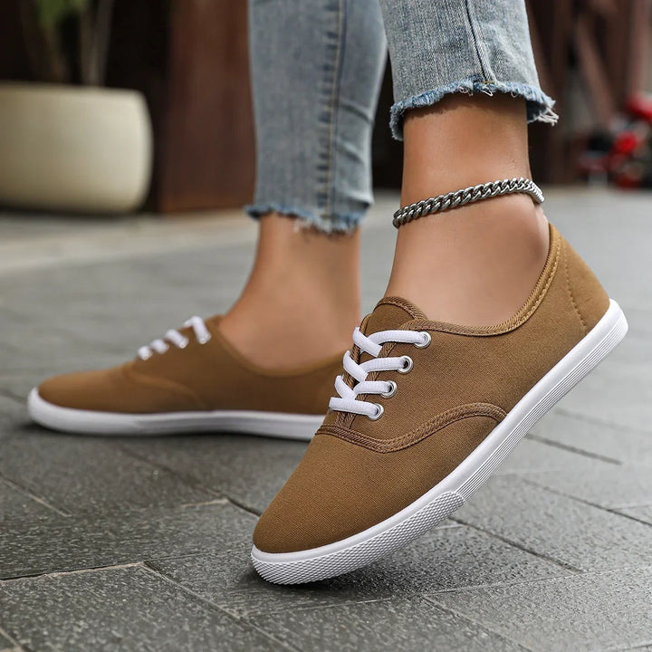 Close-up of feet wearing brown casual canvas sneakers with white laces and a silver ankle chain