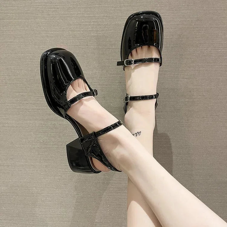 Shiny black patent leather Mary Jane heels with square toes and ankle straps on feet