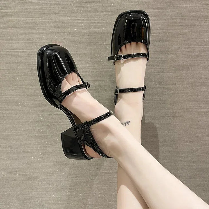 Shiny black patent leather Mary Jane heels with square toes and ankle straps on feet