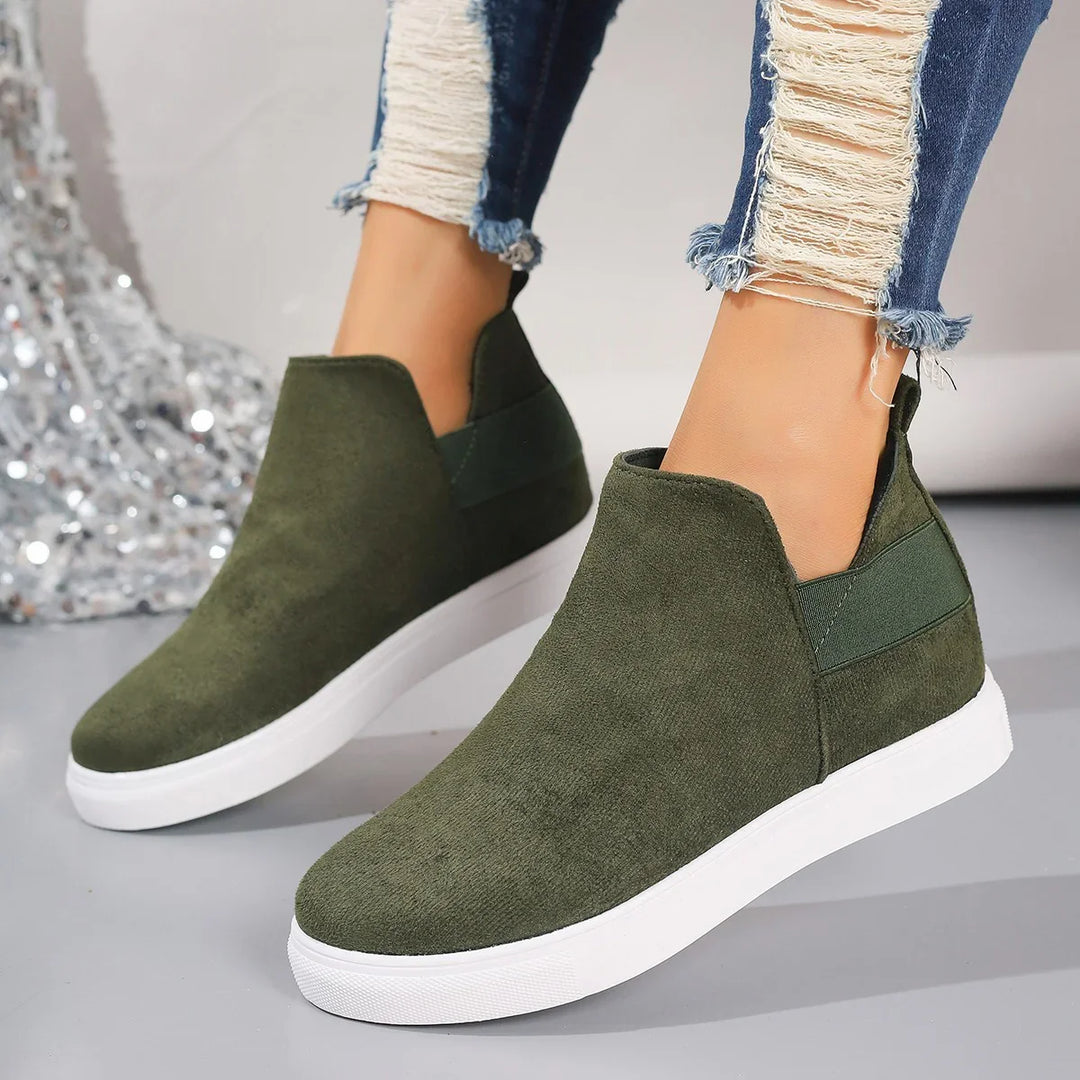 Woman wearing olive green slip-on casual sneakers with white soles and distressed blue skinny jeans