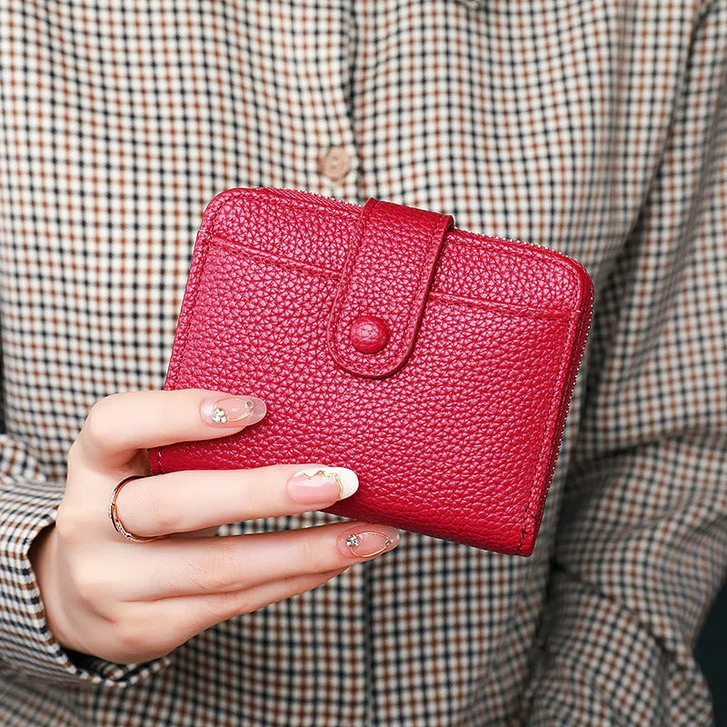 Woman holding a textured red leather wallet with button strap, wearing checkered shirt and ring