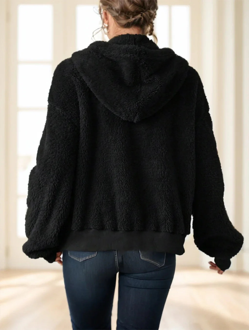 Back view of woman wearing black sherpa fleece hoodie and blue jeans in bright room